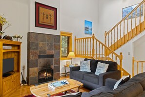 A living room with a stone fireplace, a wooden staircase, a sofa set, and a television. - Outpost: Clark's Knoll 367 - Walk to Town Square (Jackson)