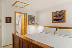 A bedroom with a wooden headboard, a bed with white linens, a nightstand with a lamp, and two framed pictures on the wall. - Outpost: Clark's Knoll 367 - Walk to Town Square (Jackson)