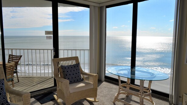 Een balkon met rieten meubels, een glazen tafel en uitzicht op de oceaan.