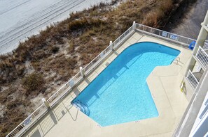 A swimming pool with a curved edge, surrounded by a white fence, and adjacent to a sandy beach area. - One Ocean Place 509 - Oceanfront in Garden City Beach (Garden City)