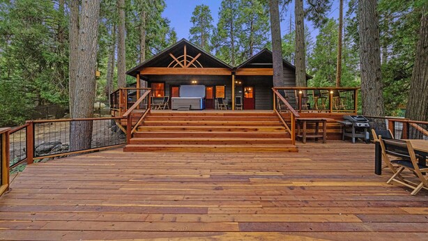 Una terraza de madera que lleva a una cabaña con un ventanal grande y una zona de barbacoa.