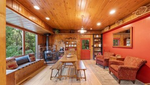 Interior acogedor de una cabaña con una mesa de comedor de madera, bancos, un sofá y una pared roja.