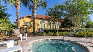 A hot tub with a metal railing, surrounded by a brick patio, with a palm tree and a yellow building in the background. - 483-Stunning 6-Bed Home w/ Private Pool, Quiet Conservation View (Davenport)
