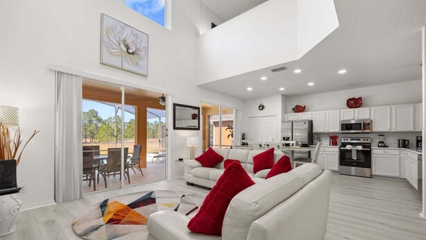 A modern living area with a sofa, a dining table, and a kitchen with white cabinets and appliances. - 483-Stunning 6-Bed Home w/ Private Pool, Quiet Conservation View (Davenport)