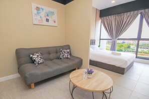 A modern hotel room with a grey sofa, a round wooden table, a bed with a white duvet, and a large window with curtains. - Bell Suites by Salaam Suites (Sepang)