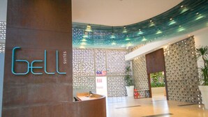 A hotel reception area with a modern design, featuring a curved reception desk, a decorative ceiling, and a patterned wall with a sign reading "Bell Suites".
