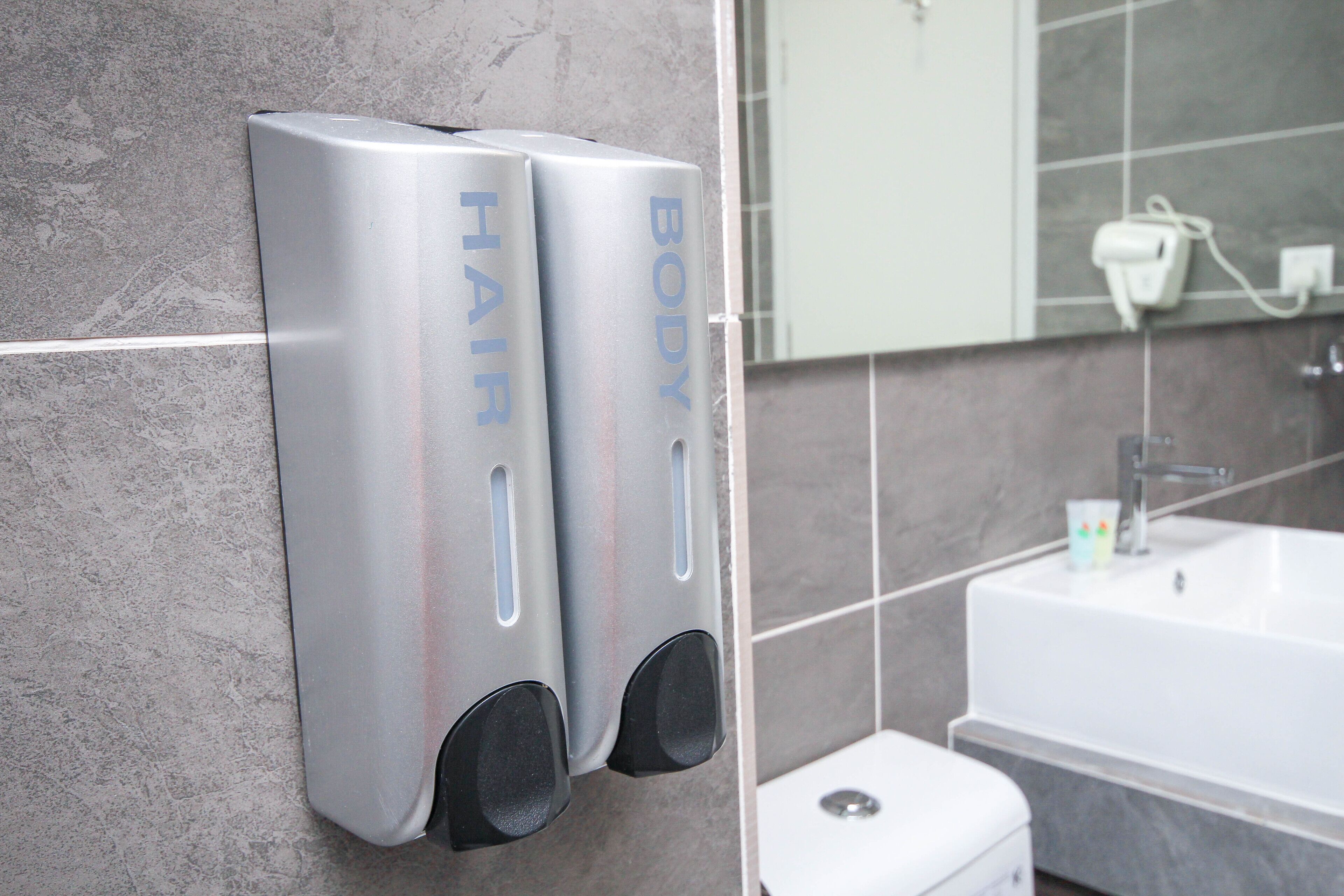 Et badeværelse med et moderne design, der inkluderer en vægmonteret dispensere til håb- og kropssæbe, et hvidt badekar og et toilet.