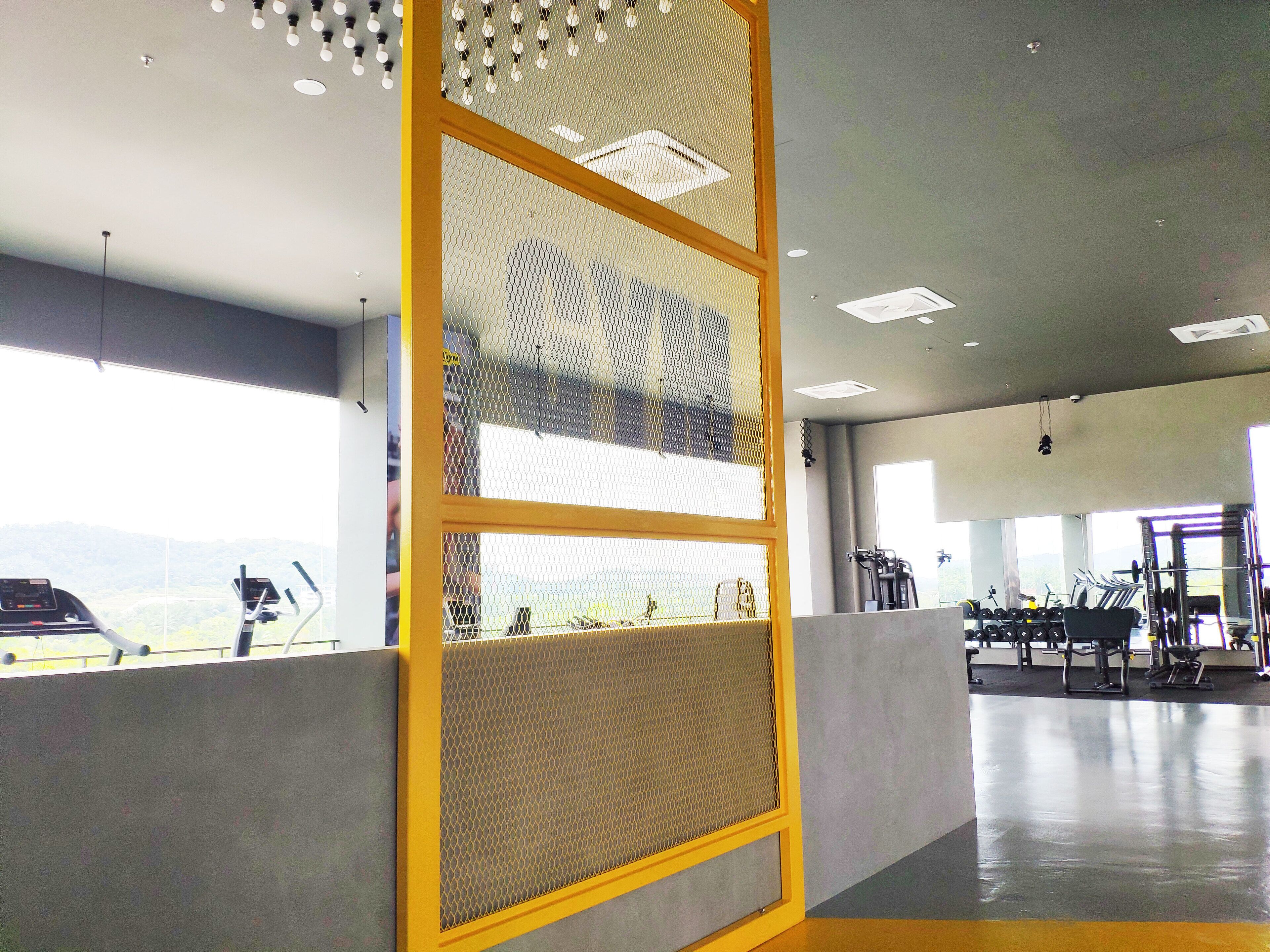 A gym with exercise equipment, a large window, and a yellow partition.