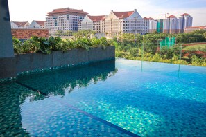 A clear blue pool with a tiled edge, surrounded by greenery and buildings in the background. - Bell Suites by Salaam Suites (Sepang)