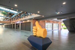 A spacious indoor area with a large thumbs-up sculpture, a 7-Eleven store, and a brick wall. - Bell Suites by Salaam Suites (Sepang)