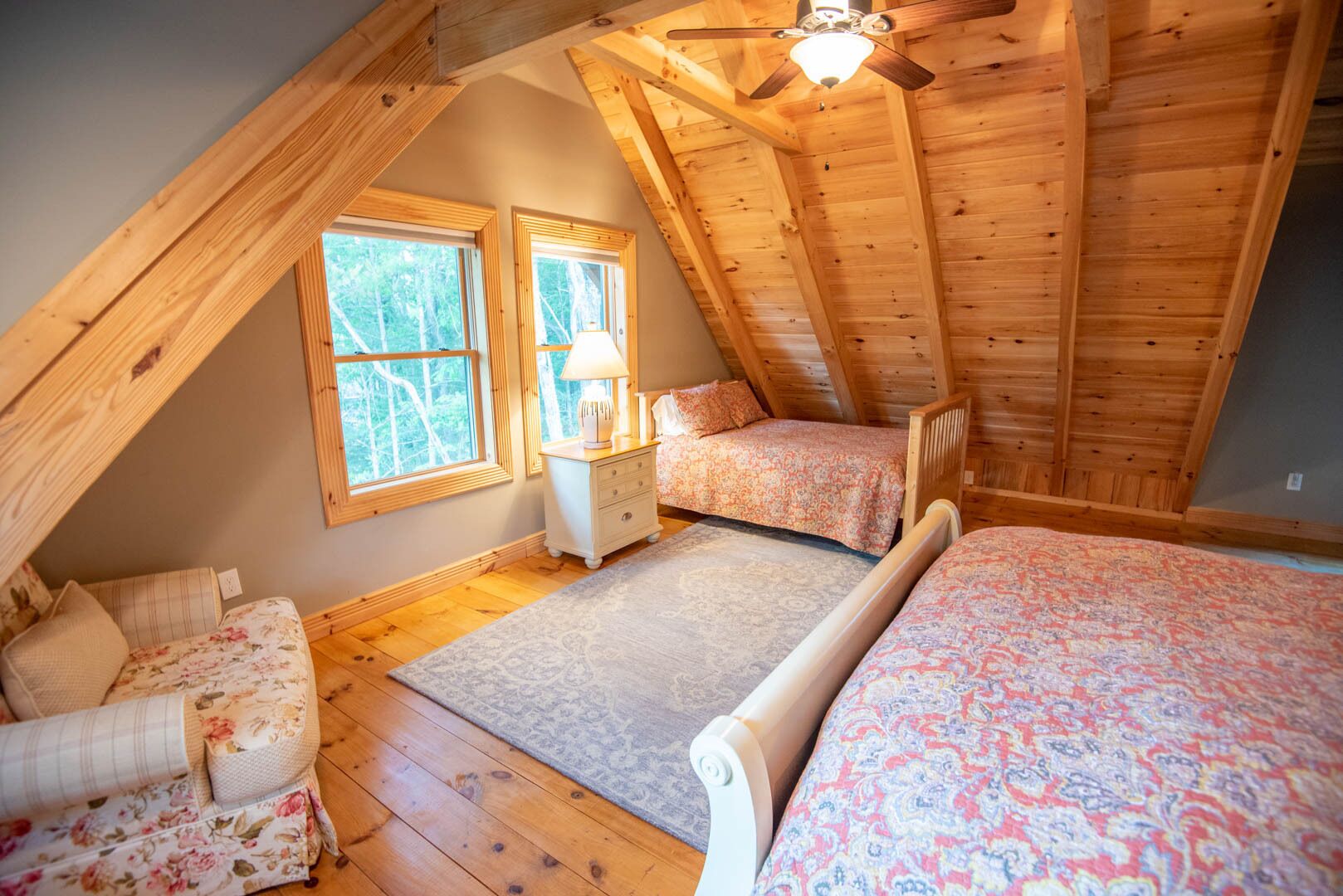 A cozy attic bedroom with two beds, a nightstand, and a ceiling fan.