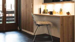 Un interior moderno con una puerta de madera, una silla negra con cojín de piel, una estantería con objetos decorativos y un televisor de pantalla plana montado sobre la estantería.