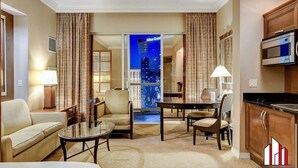 A hotel room with a sofa, armchairs, a dining table, and a kitchen area.