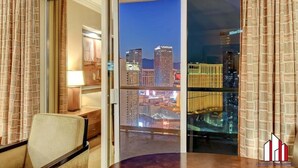 A hotel room with a city view, a desk with a lamp, and a chair.