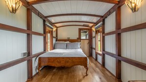A wooden-framed bedroom with a bed, wooden floor, and wall-mounted light fixtures. - The Railway Carriage, Melton Constable, Norfolk (Melton Constable)