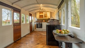 A spacious kitchen with wooden flooring, a central island, and large windows offering views of the outdoors. - The Railway Carriage, Melton Constable, Norfolk (Melton Constable)