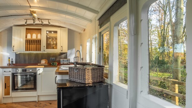 A kitchen with white cabinets, a black refrigerator, and a window overlooking a garden. - The Railway Carriage, Melton Constable, Norfolk (Melton Constable)