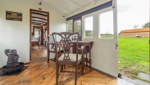A wooden dining table with chairs, a notice board, and a view of a green field through a door. - The Railway Carriage, Melton Constable, Norfolk (Melton Constable)