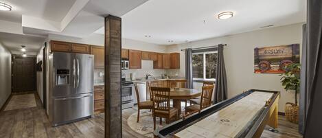 A modern kitchen with wooden cabinets, stainless steel appliances, and a pool table.