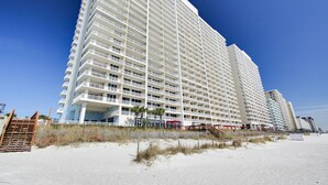 A high-rise hotel with multiple balconies, located near a sandy beach.