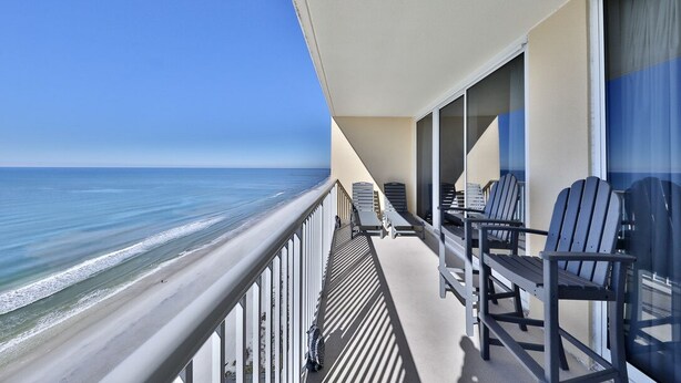 A balcony with a view of the ocean, featuring a railing and several Adirondack chairs.