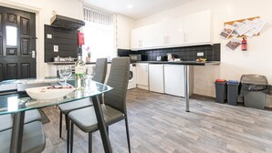 Una cocina moderna con armarios blancos, una encimera negra y una mesa de comedor de vidrio con sillas. Se aprecia el logo de North West Accommodation y un cartel de Viro.