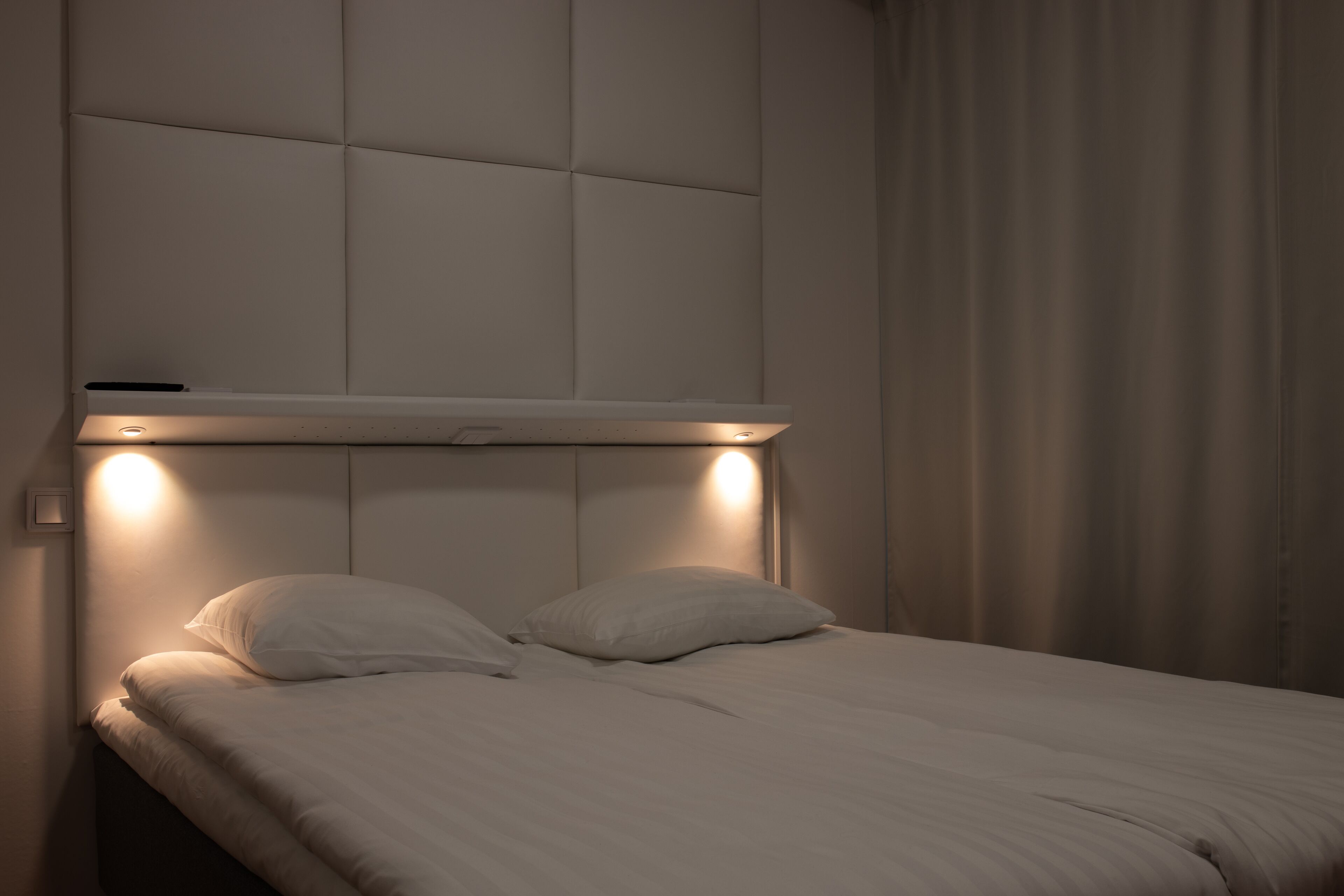 A bed with a headboard, two pillows, and a bedside table with a light.
