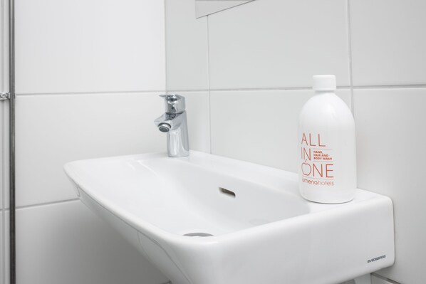 A white bathroom sink with a chrome faucet and a bottle of hand soap labeled "ALL IN ONE" on the right side.