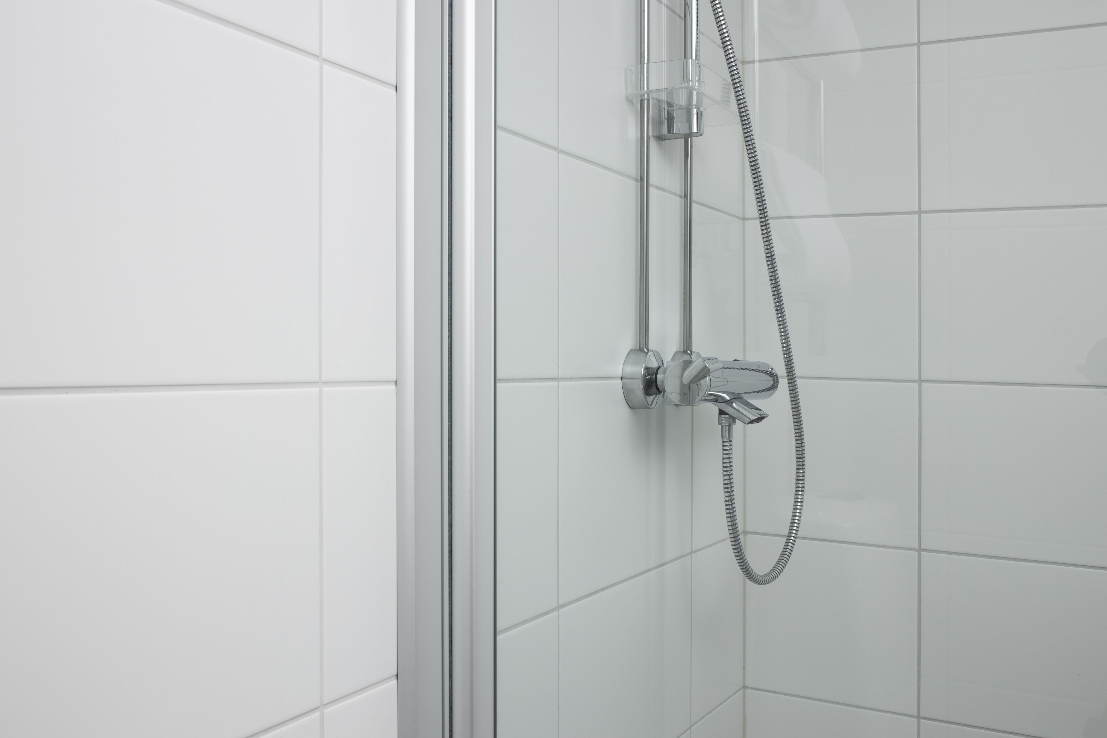 A modern bathroom with white tiled walls and a glass shower enclosure.