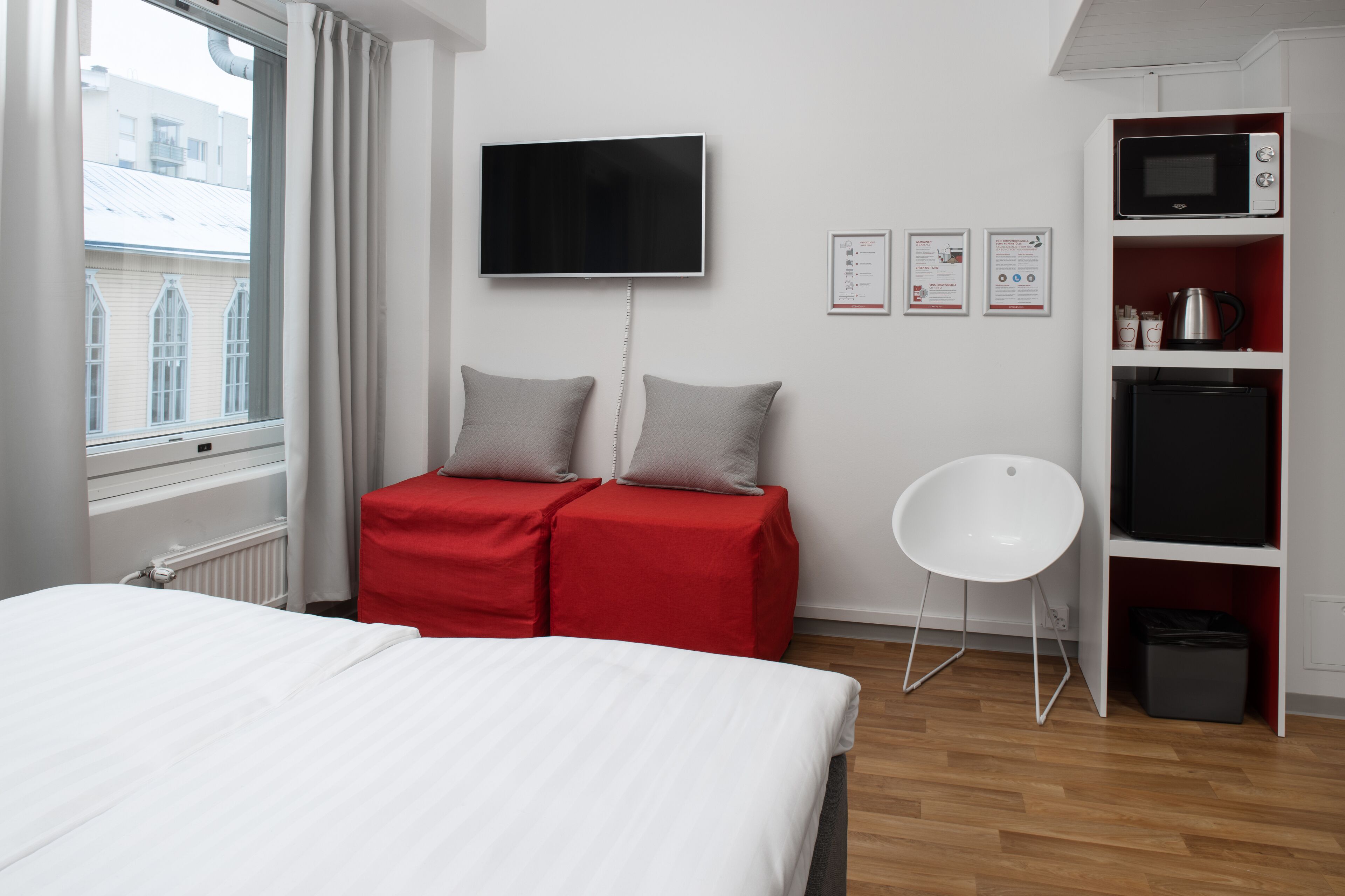 A hotel room with a bed, a red sofa, a TV, a microwave, and a small white chair.