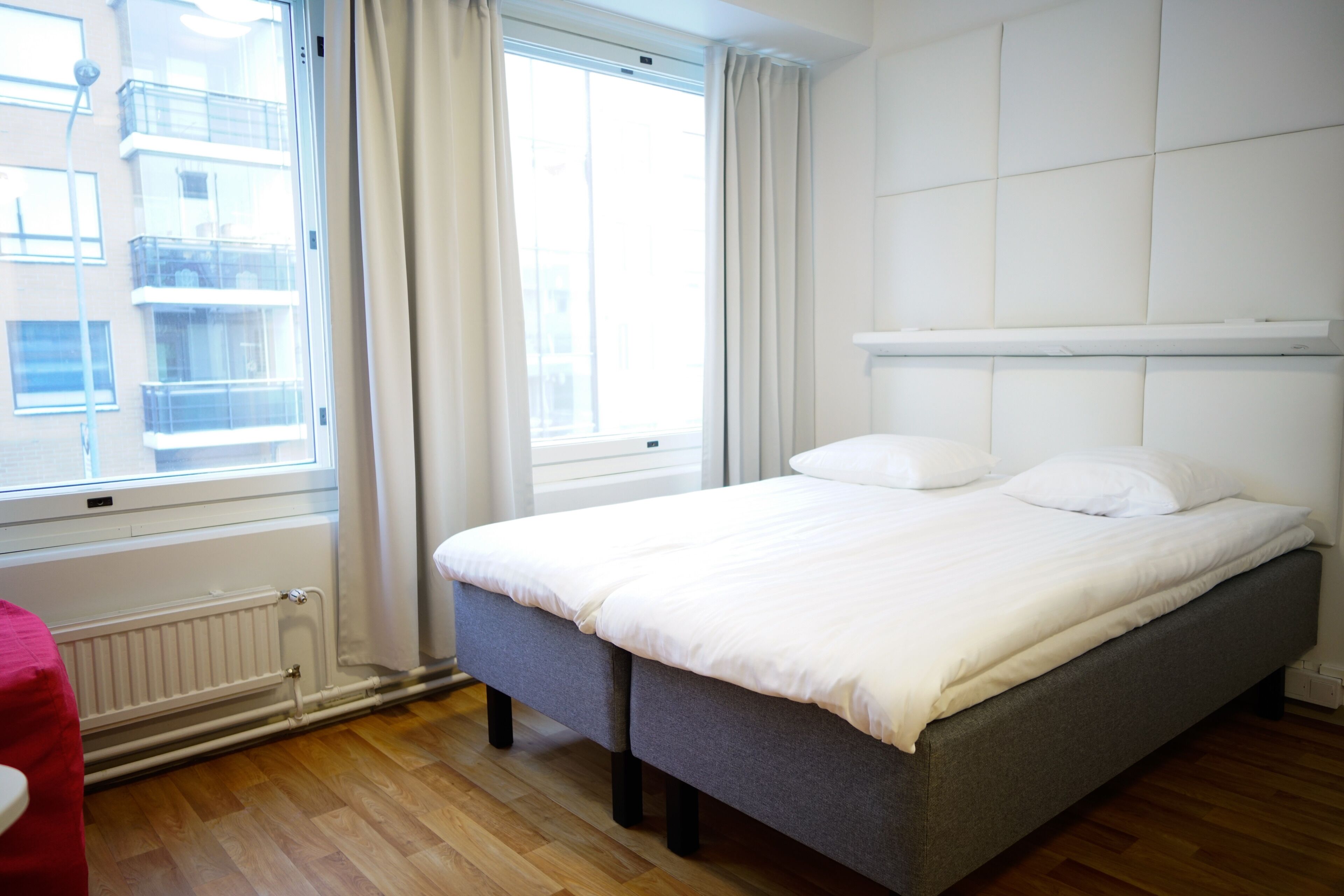 A neatly made bed in a room with a window, a radiator, and a wooden floor.