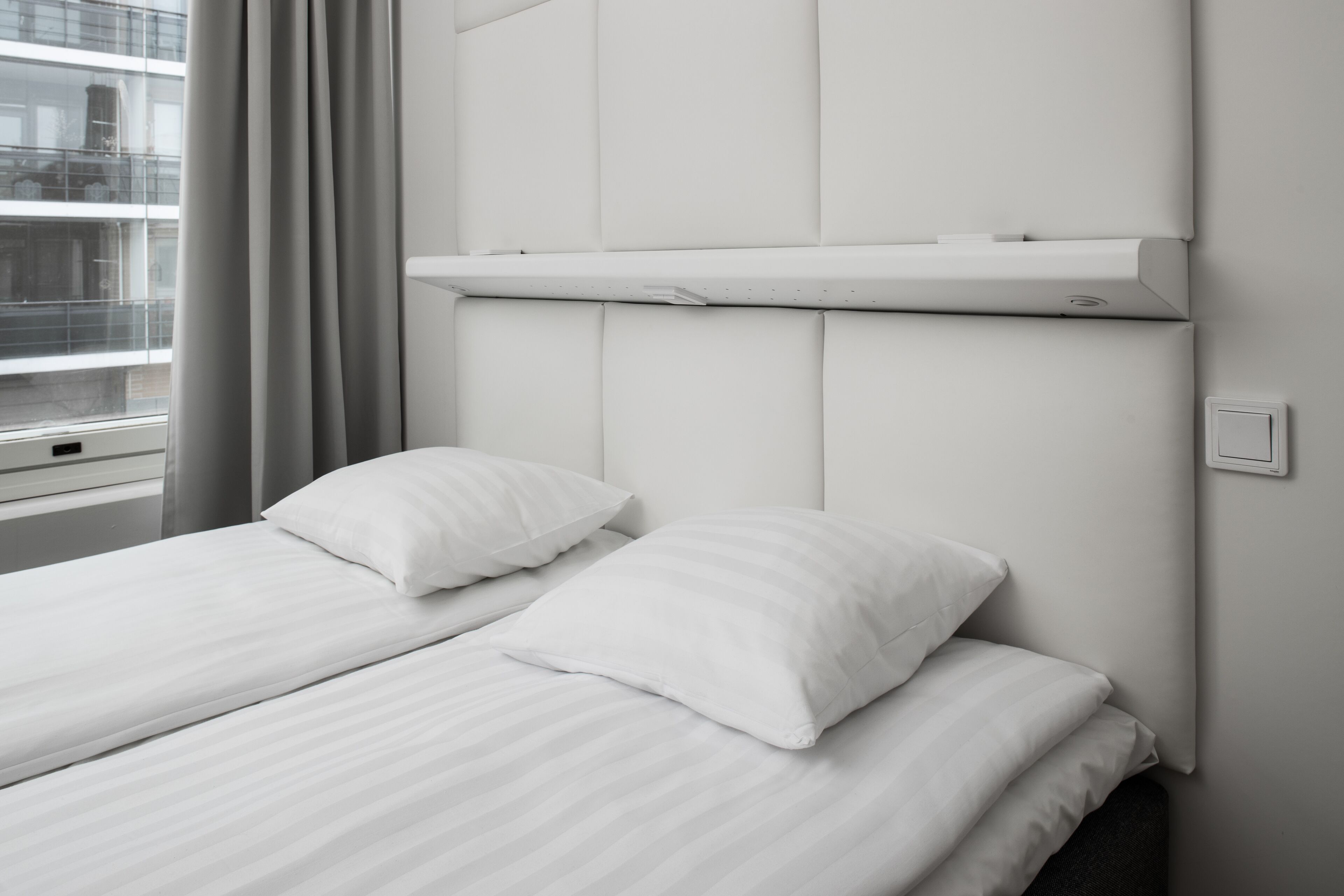 Una camera d'albergo con un letto, cuscini, una finestra con tende e un condizionatore d'aria a muro.