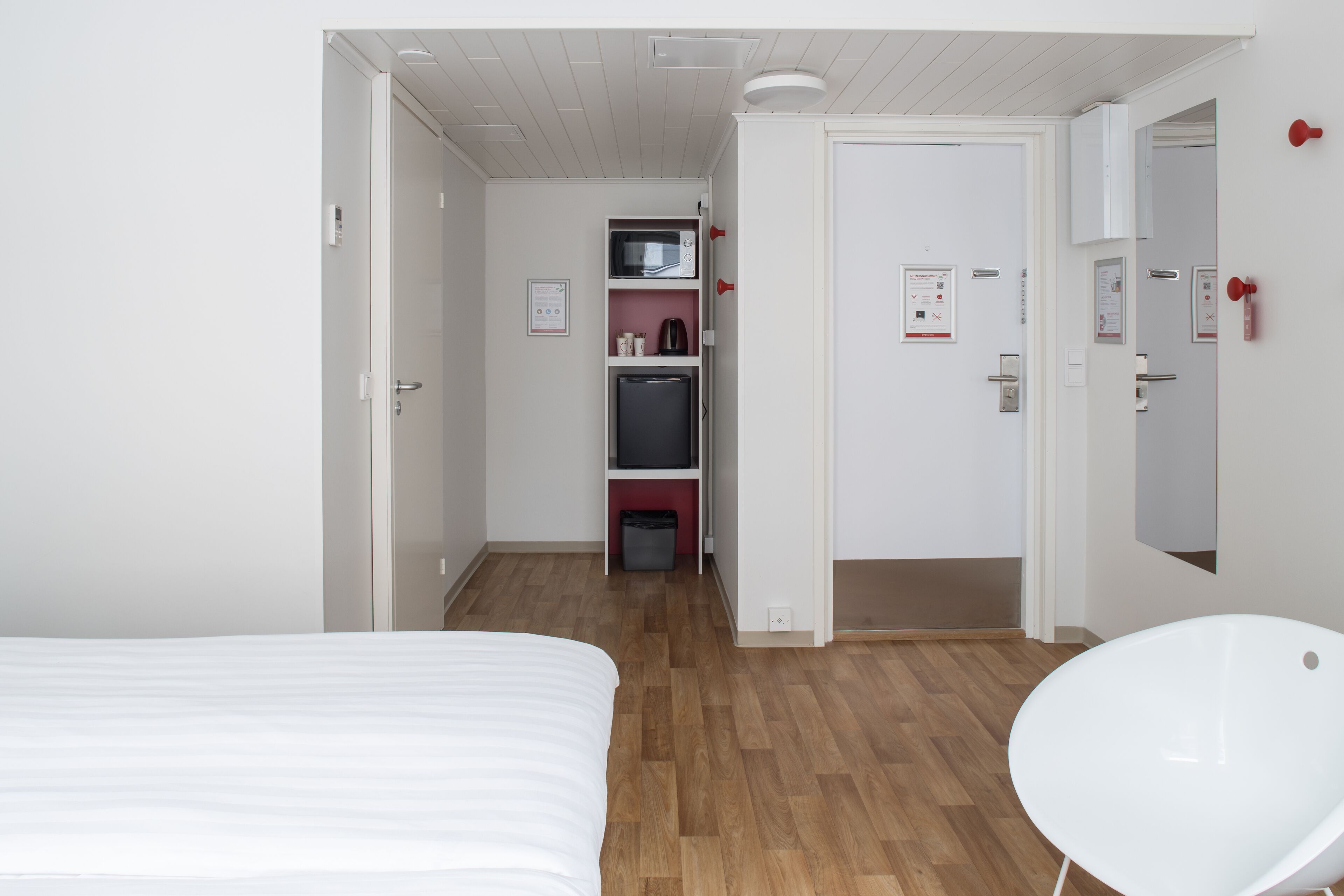A hotel room with a bed, a white chair, a microwave, a refrigerator, and a small kitchenette area.