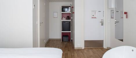 A hotel room with a bed, a white chair, a microwave, a refrigerator, and a small kitchenette area.