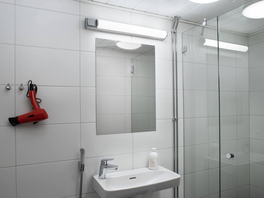 A bathroom with a white sink, a mirror, and a red hairdryer on the wall.