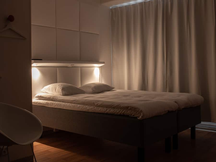 A bedroom with a bed, a chair, a bedside table, and a window with curtains.