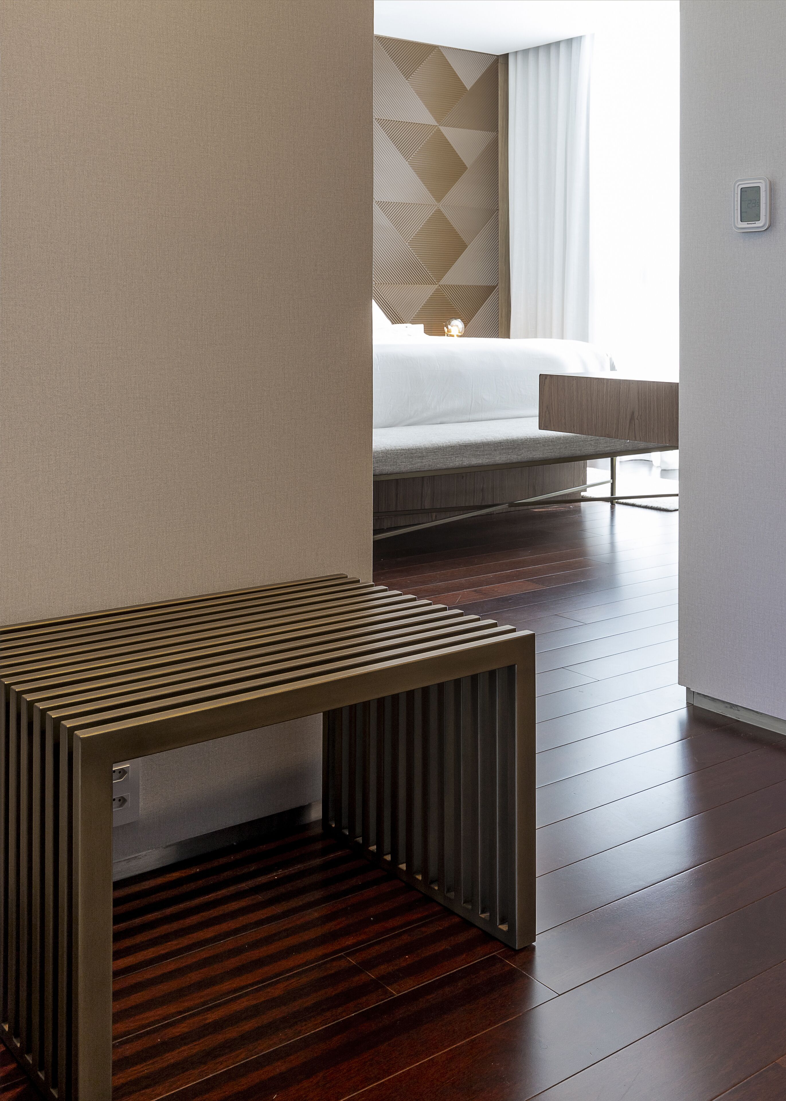 A hotel room with a bed, a bedside table, and a wooden floor.