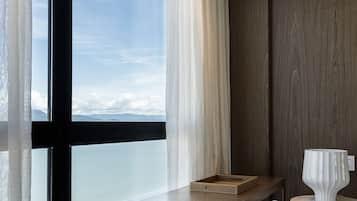Una habitación de hotel moderna con un ventanal grande, un escritorio de madera, una silla y una mesita con una lámpara.