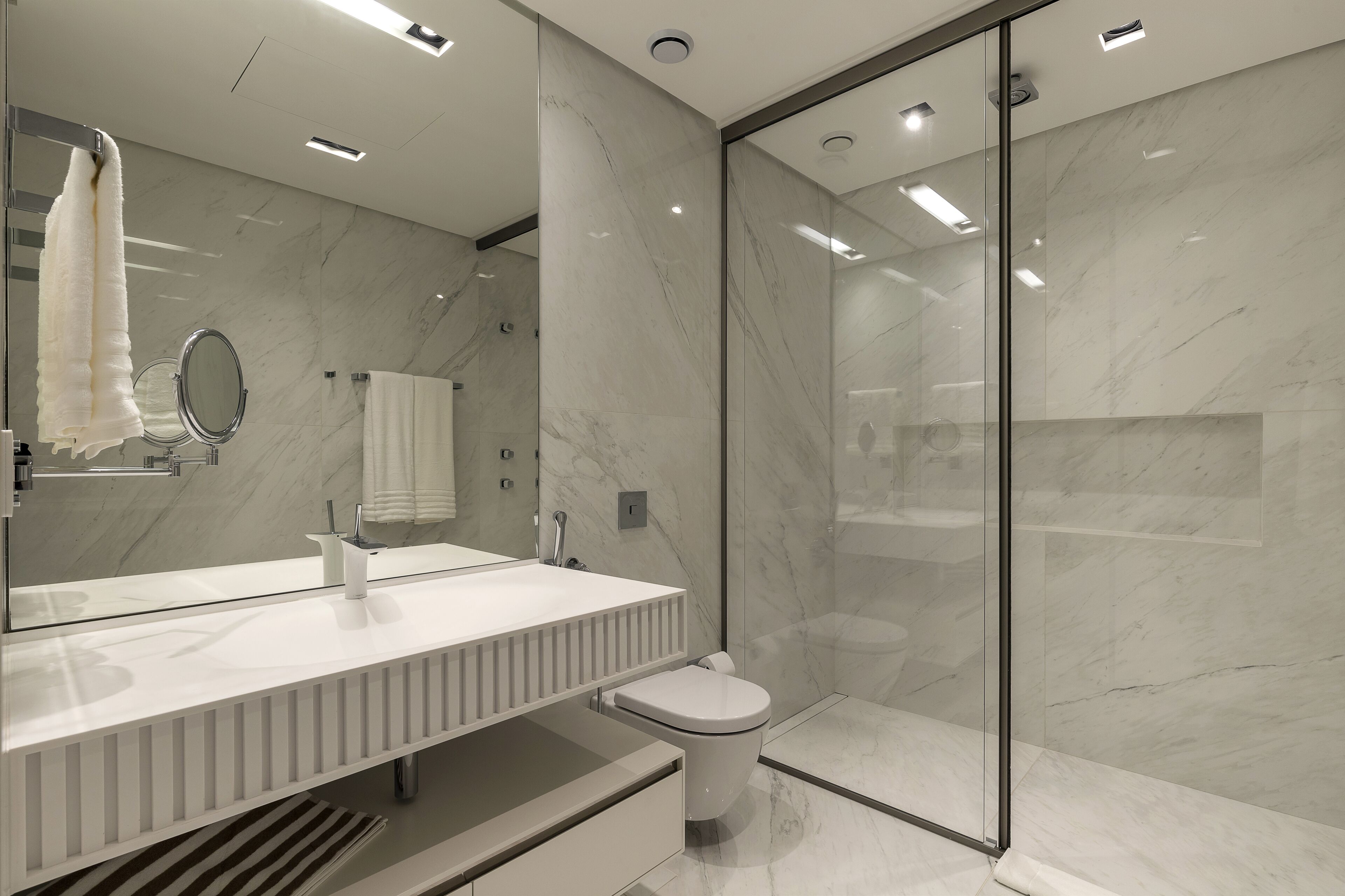 Un baño moderno con cabina de ducha de vidrio, inodoro blanco y tocador con espejo.