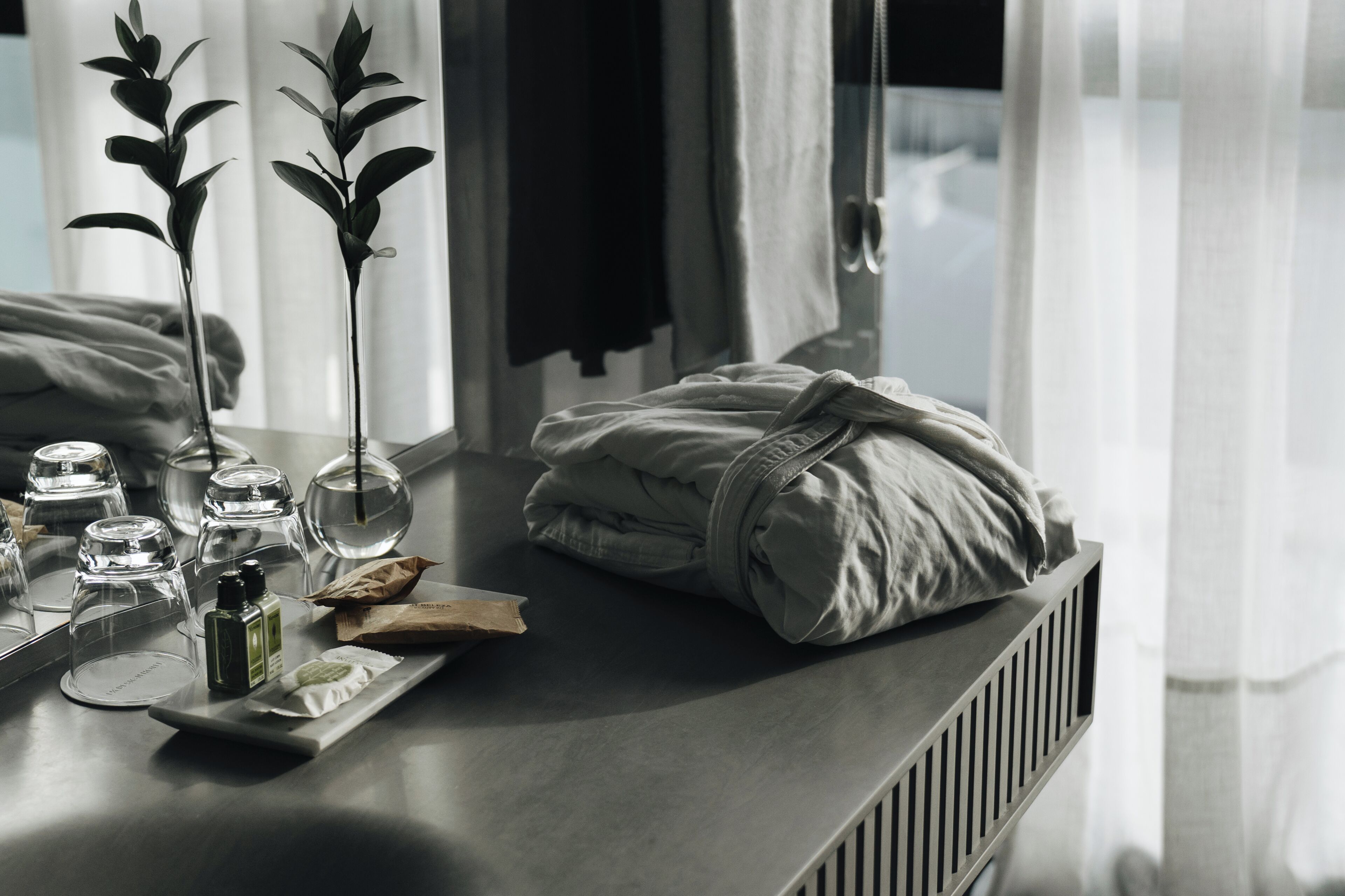 Habitación ordenada con una cama, una mesita de noche con un atril de artículos de tocador y un espejo que refleja el cuarto.
