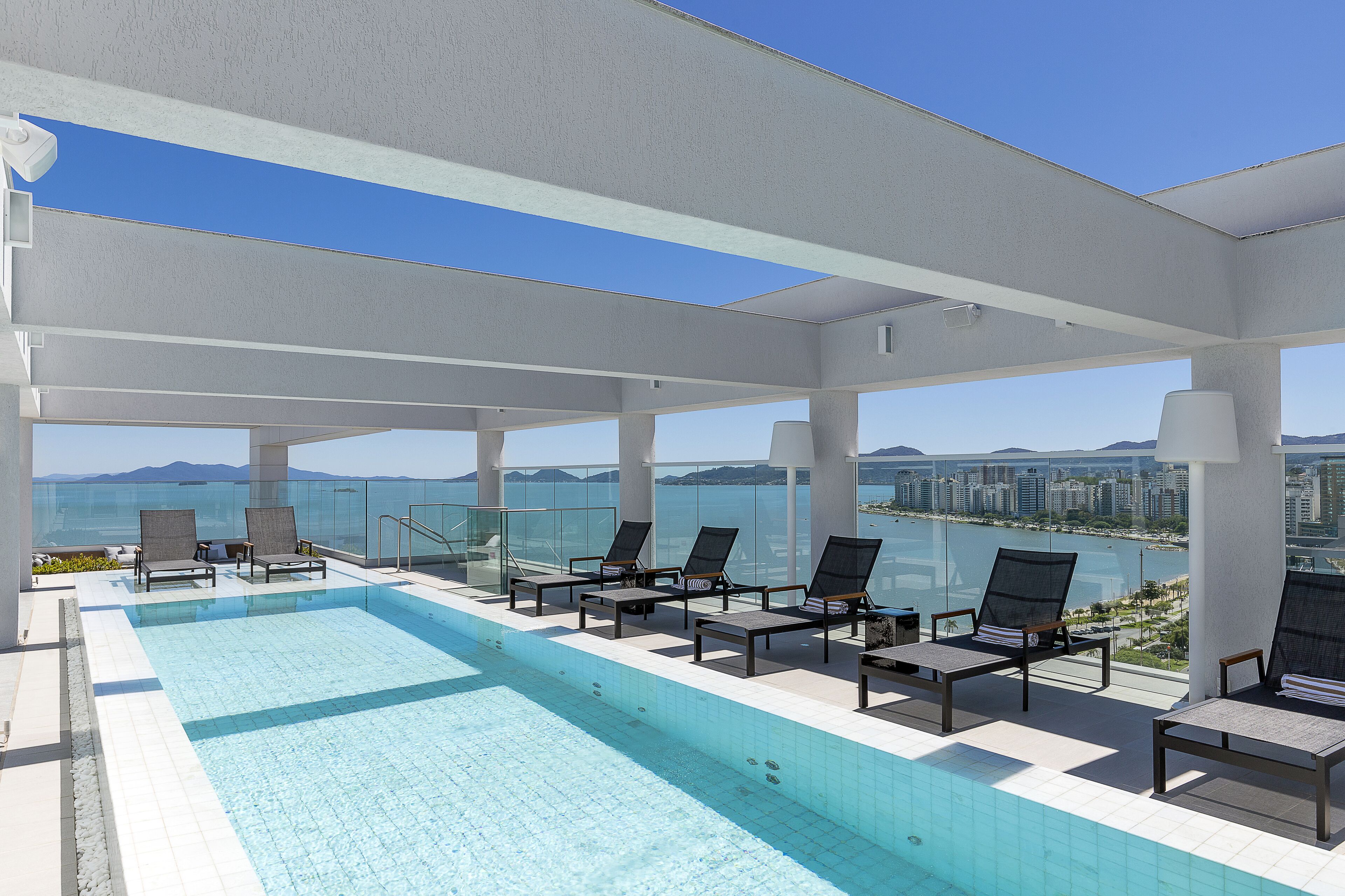 Une piscine à débordement située sur le toit, avec des chaises longues et une vue sur la ville.