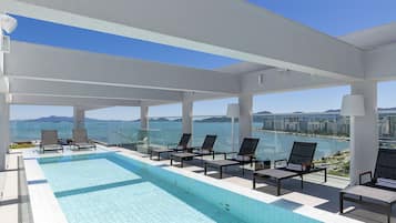 Une piscine à débordement située sur le toit, avec des chaises longues et une vue sur la ville.