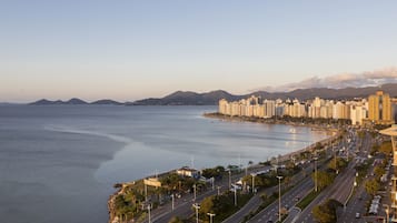 A coastal cityscape with a wide road, buildings, and a calm sea.