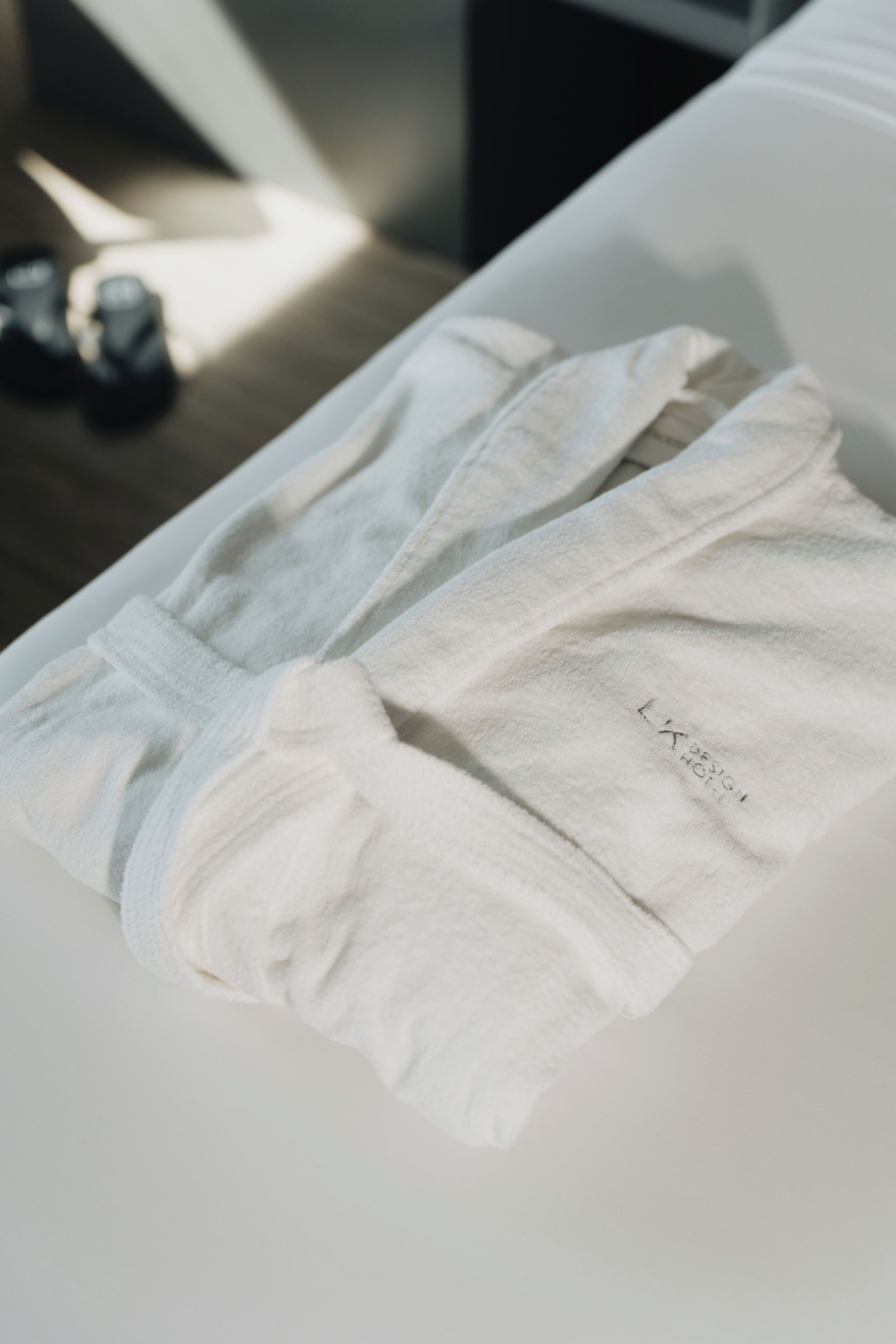 A neatly folded white towel with a logo on a white surface, likely in a hotel room.