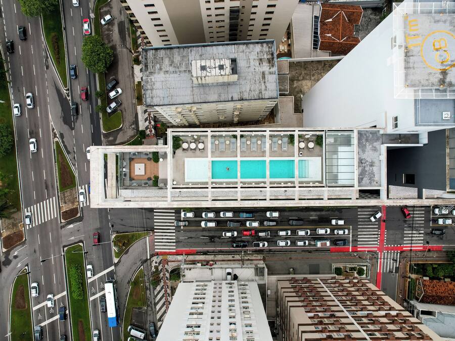 Vista aérea de un edificio moderno con piscina en la azotea, varios pisos y una calle concurrida abajo.