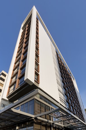 A modern high-rise building with a prominent white facade, multiple floors, and a mix of glass and wooden elements.