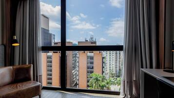 A hotel room with a large window, a sofa, a desk, and a lamp.