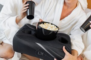 A person holding a black tray with a bowl of popcorn and a black cup, wearing a white robe.