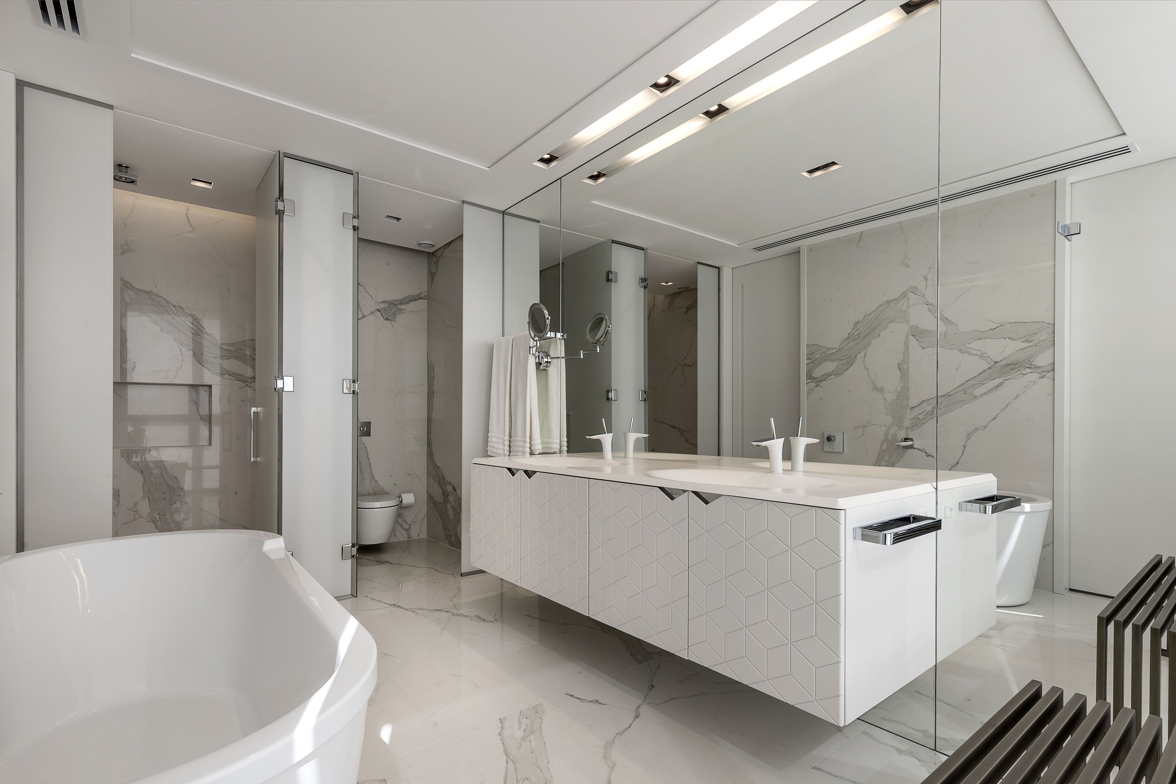 A modern bathroom with a freestanding bathtub, a large mirror, and a vanity with a geometric tile backsplash.