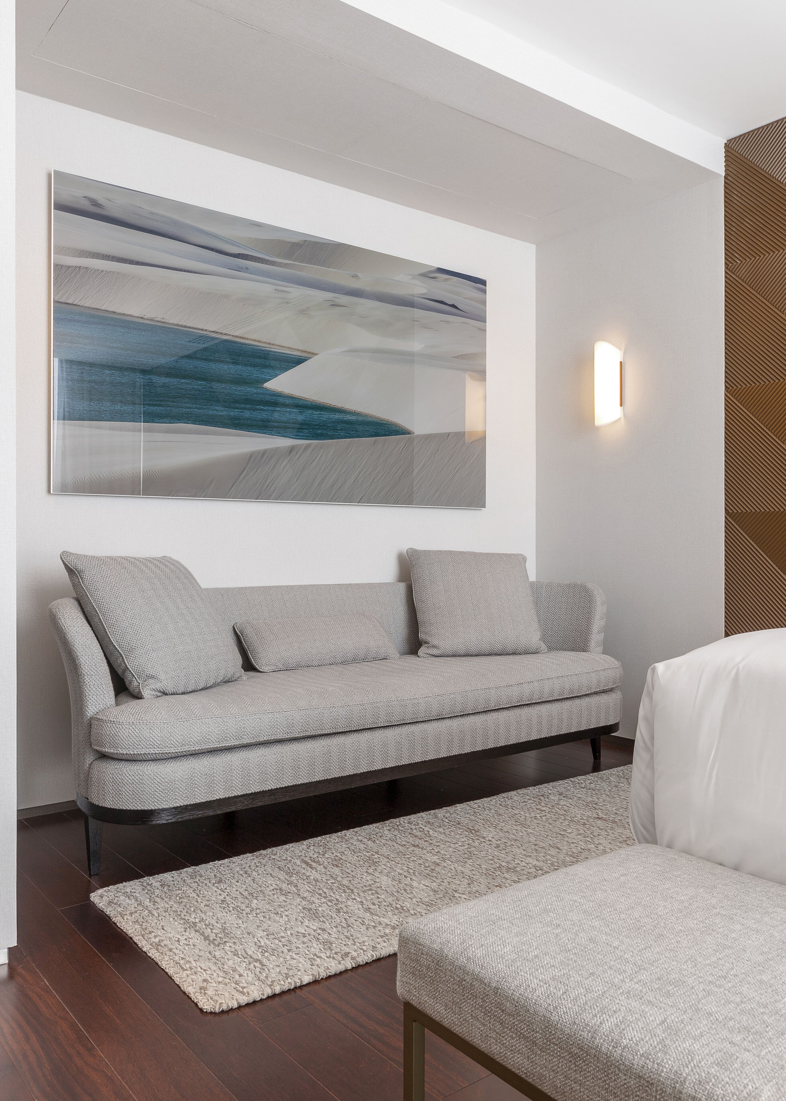 A modern living room with a grey sofa, a white armchair, a large abstract painting, and a textured rug.